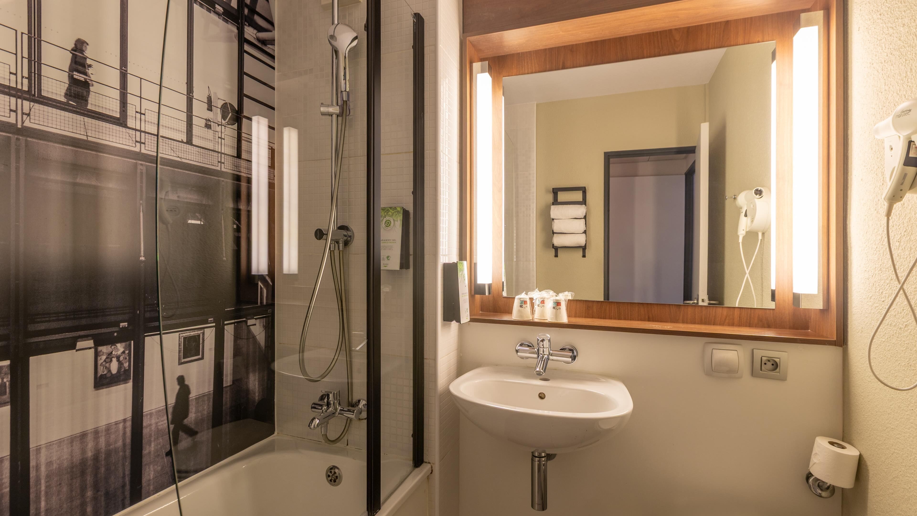 Un bagno con doccia, lavandino, specchio e porta asciugamani.