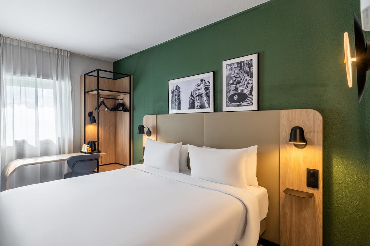 Une chambre d’hôtel comprenant un lit, un bureau, une armoire et deux tableaux accrochés au mur.
