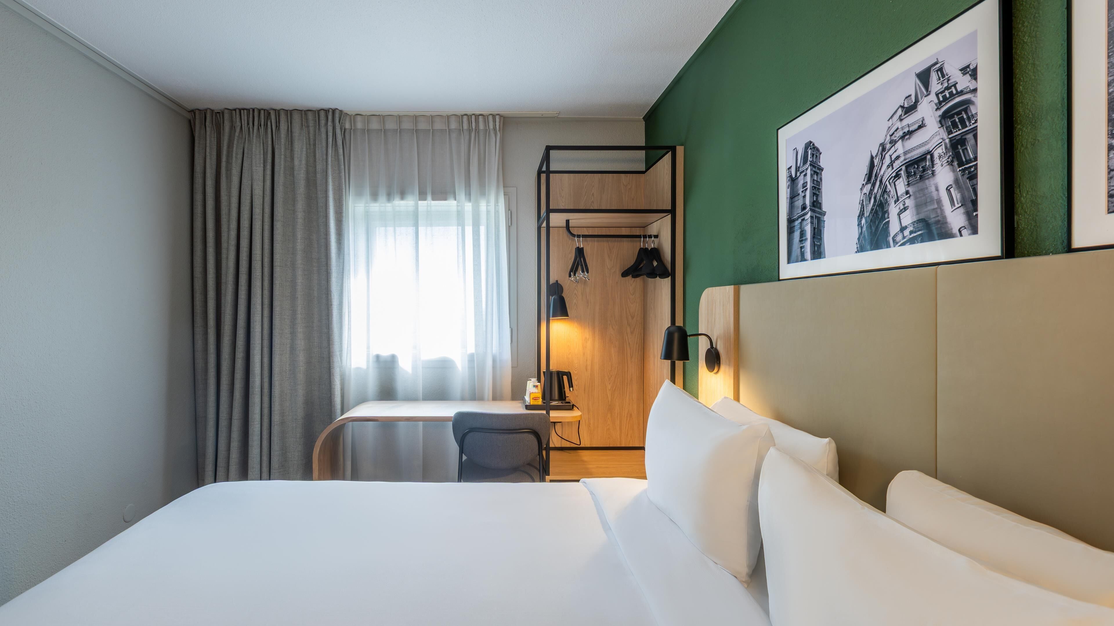Una habitación de hotel con una cama, un escritorio con una silla, una cafetera y un cuadro en la pared.