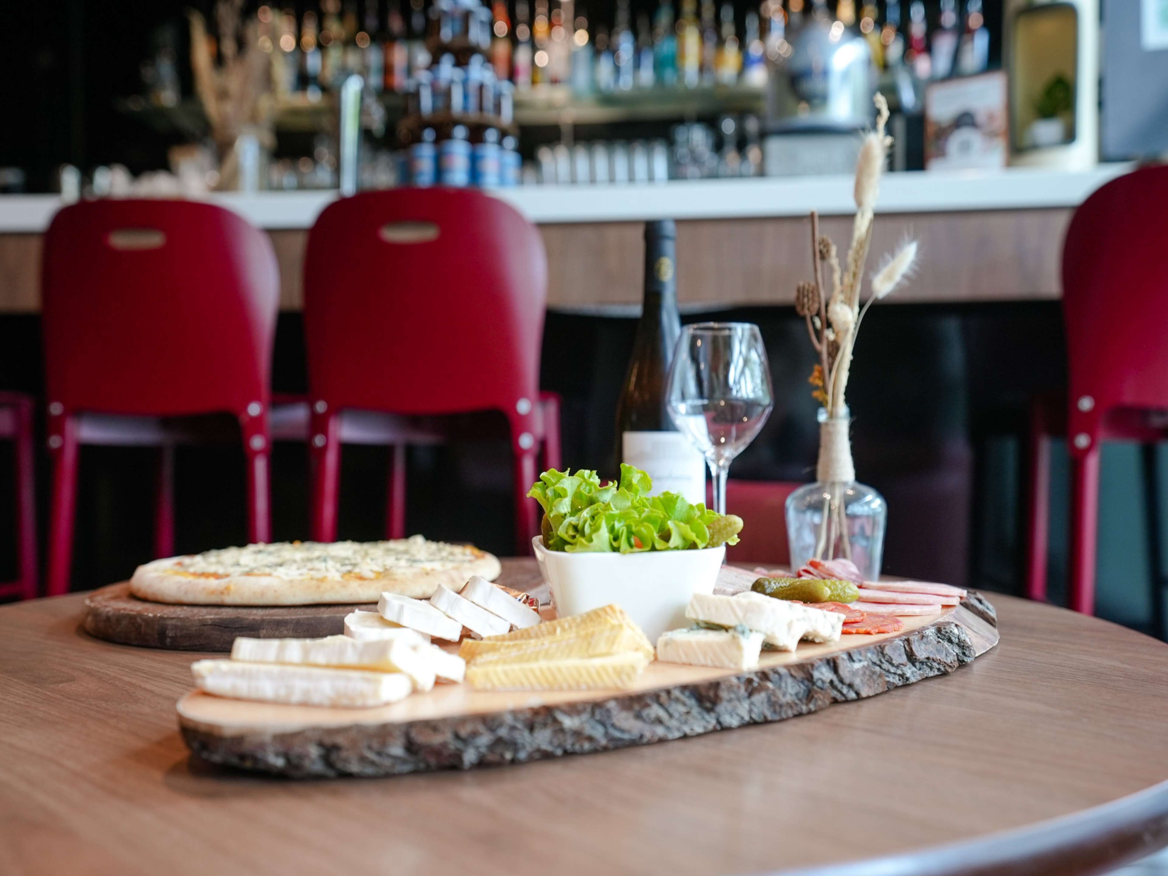 A table with a cheese board, a bowl of salad, and a bottle of wine in a restaurant setting.
