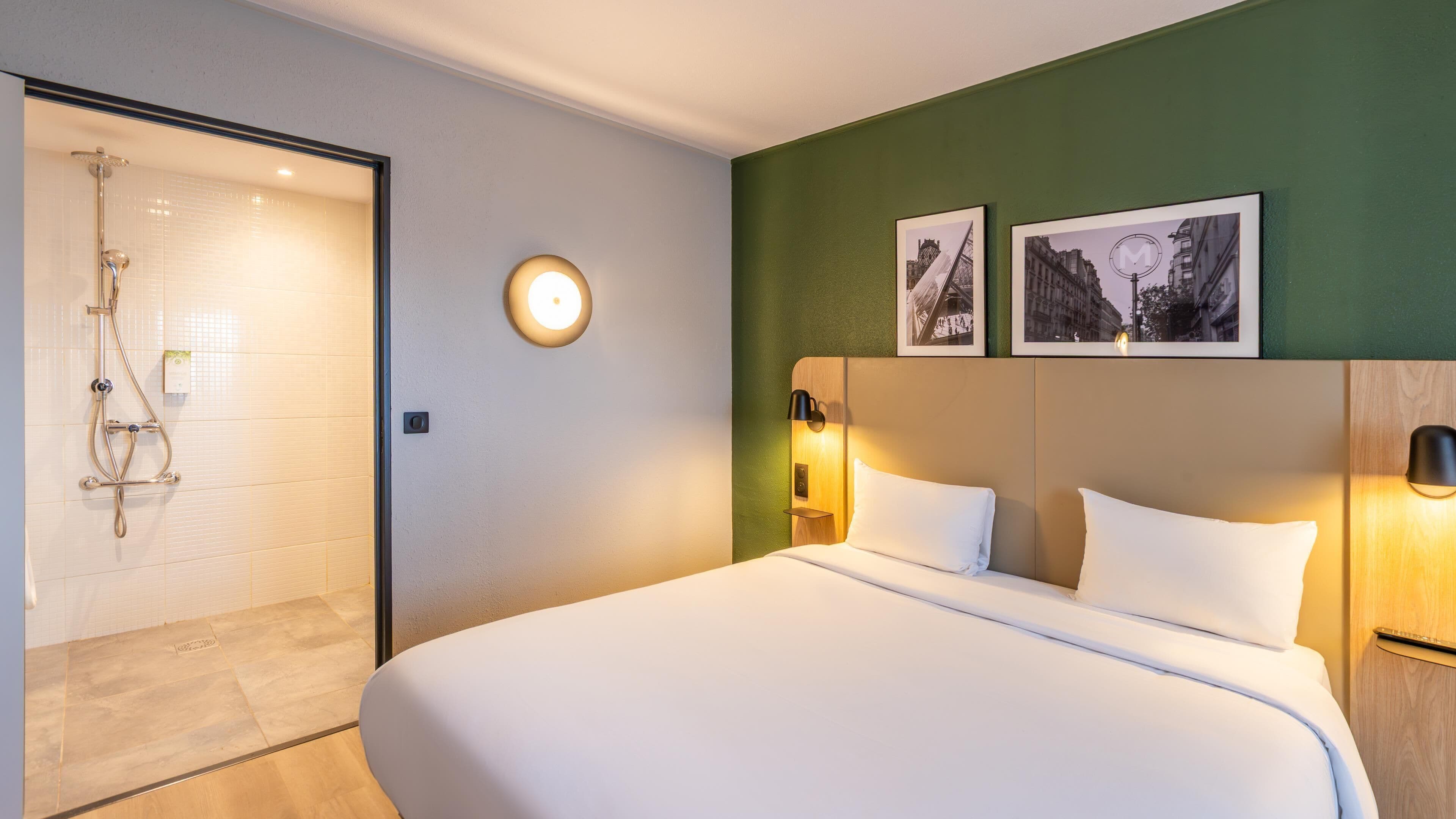 A hotel room with a bed, a shower, and two framed pictures on the wall.
