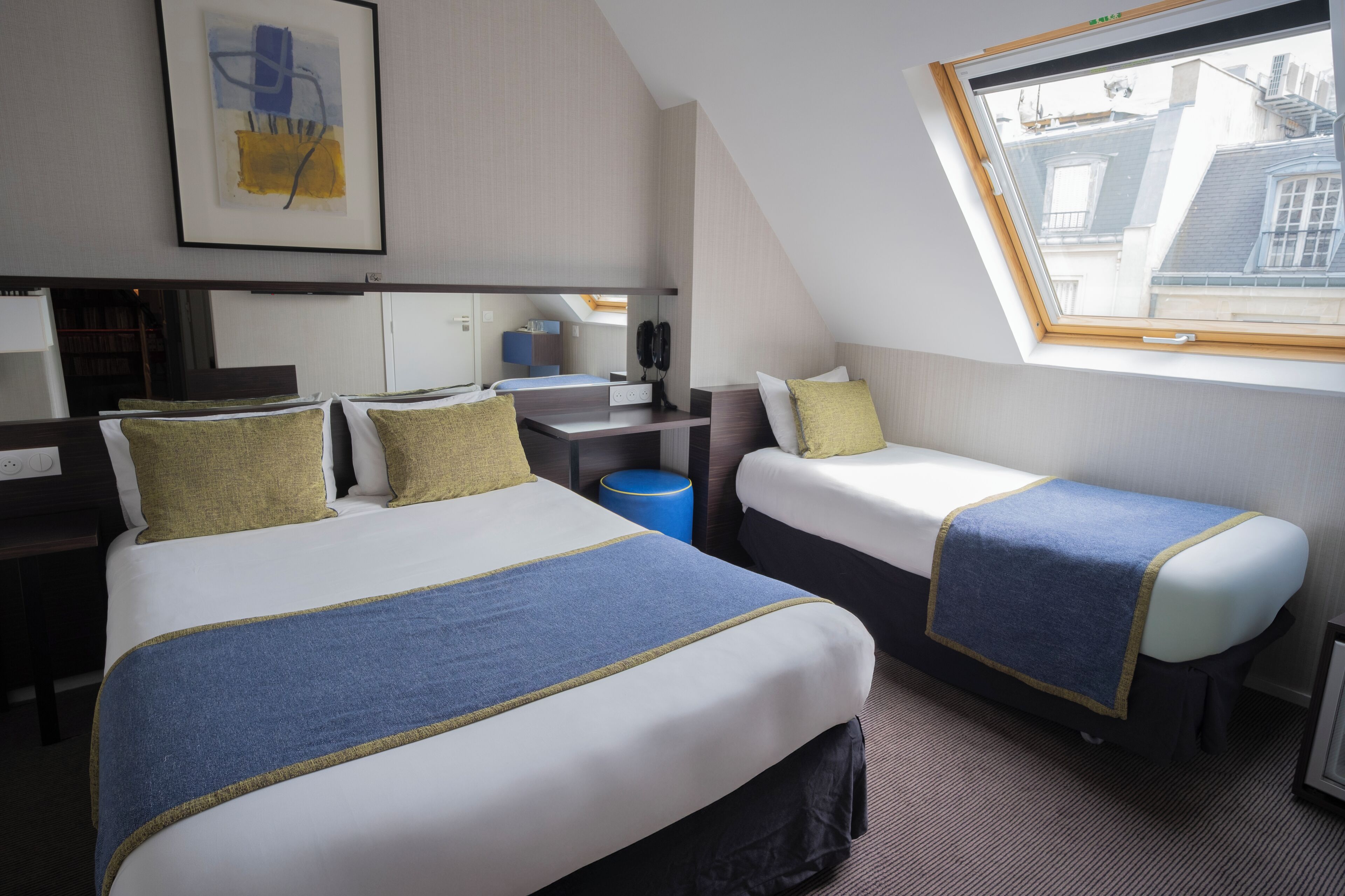 A hotel room with two beds, a desk, a chair, a telephone, and a window with a view of buildings.