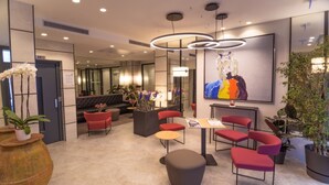 Um hall de hotel moderno, com assentos vermelhos, uma grande pintura abstrata e um vaso grande com flores.