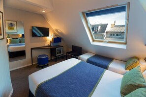 Habitación de hotel con dos camas, un escritorio, un televisor y ventana con vista a edificios.
