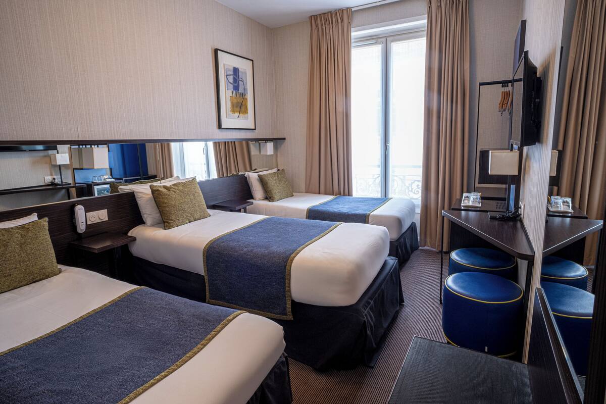 Ein Hotelzimmer mit zwei Betten, einem Schreibtisch, einem Fernseher und einem Balkon mit Vorhängen.