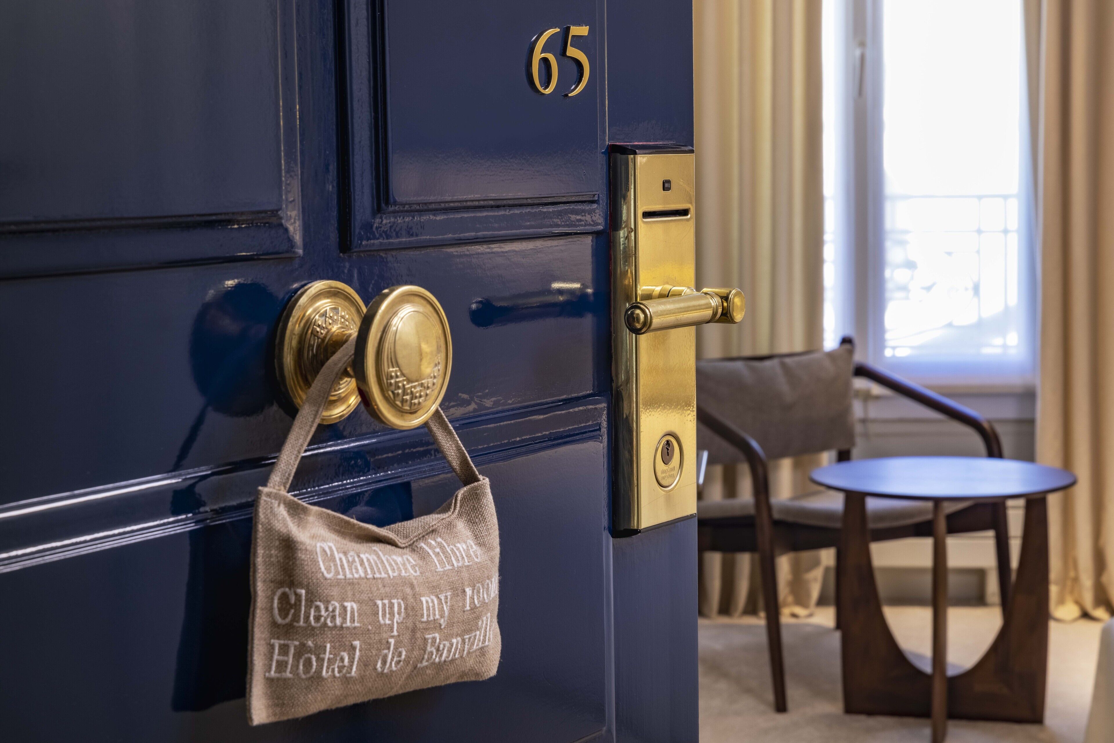 Puerta de habitación de hotel con manija de latón, un candado dorado y el número 65 encima.