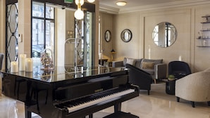 A grand piano in a well-lit living area with a modern chandelier, comfortable seating, and a large mirror on the wall. - Hôtel de Banville (Paris)