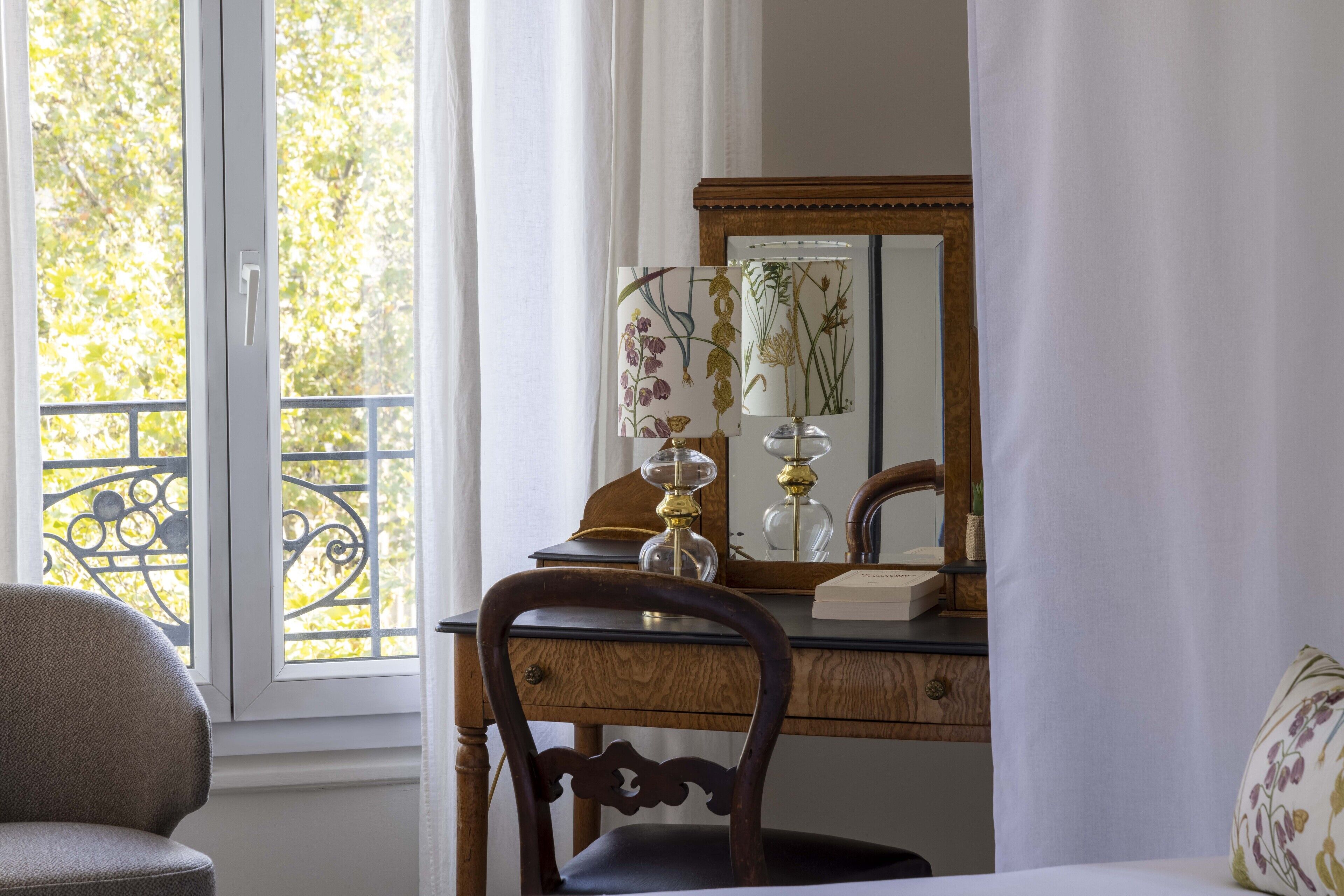 A room with a wooden desk, a chair, a mirror, and a window with a view of trees.