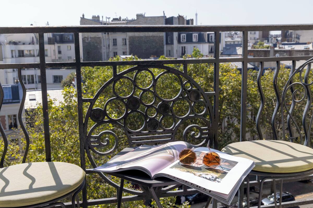 A balcony with a metal railing, a chair, a cushion, and a magazine with sunglasses on it.