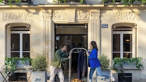 A building with a number 166 sign, a metal cart with a bag, and outdoor seating with plants. - Hôtel de Banville (Paris)