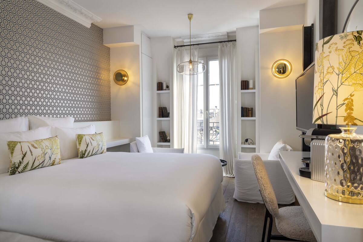 A hotel room with a large bed, a desk, a chair, a TV, and a bookshelf.