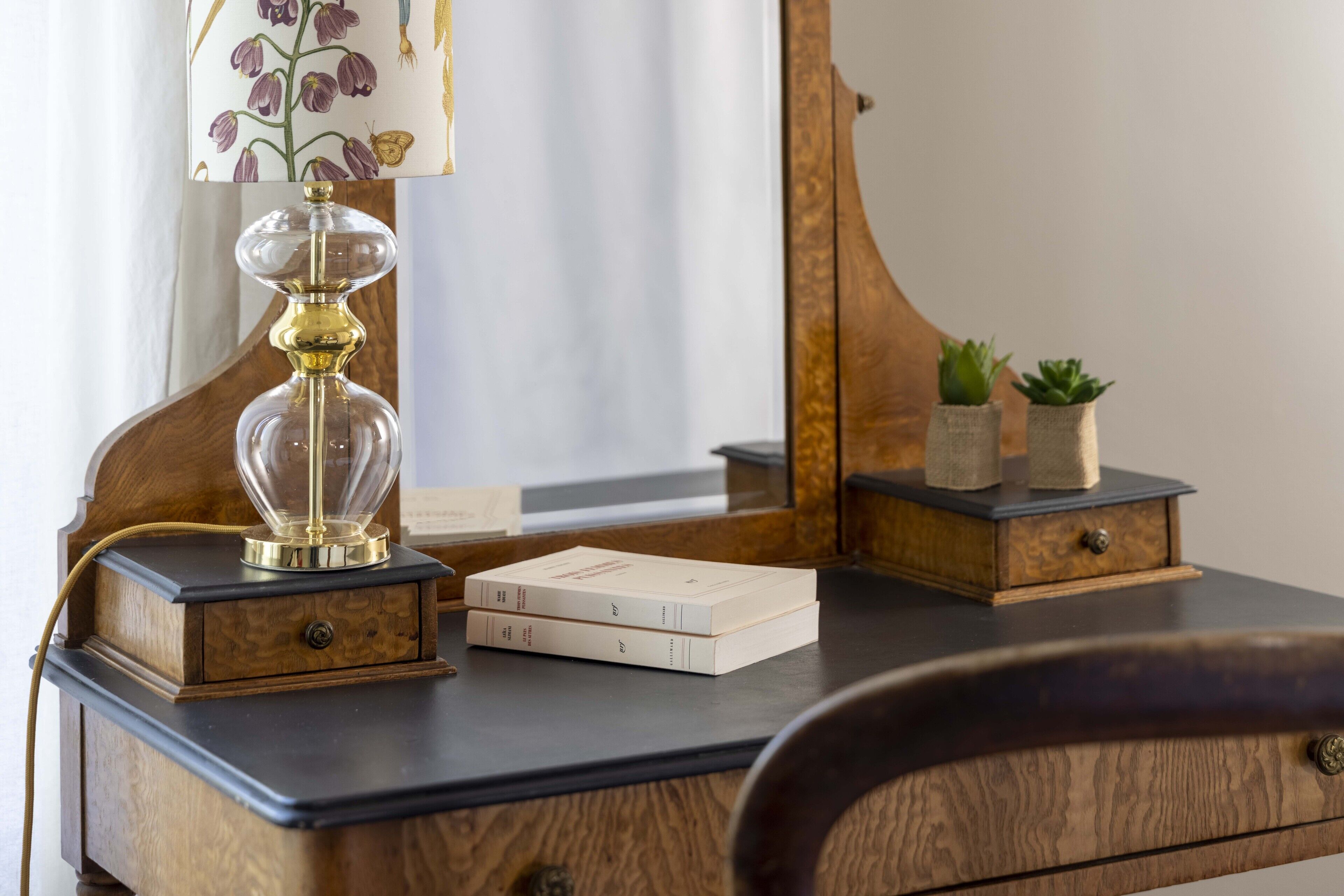 A wooden desk with a lamp, books, a mirror, and a small plant.
