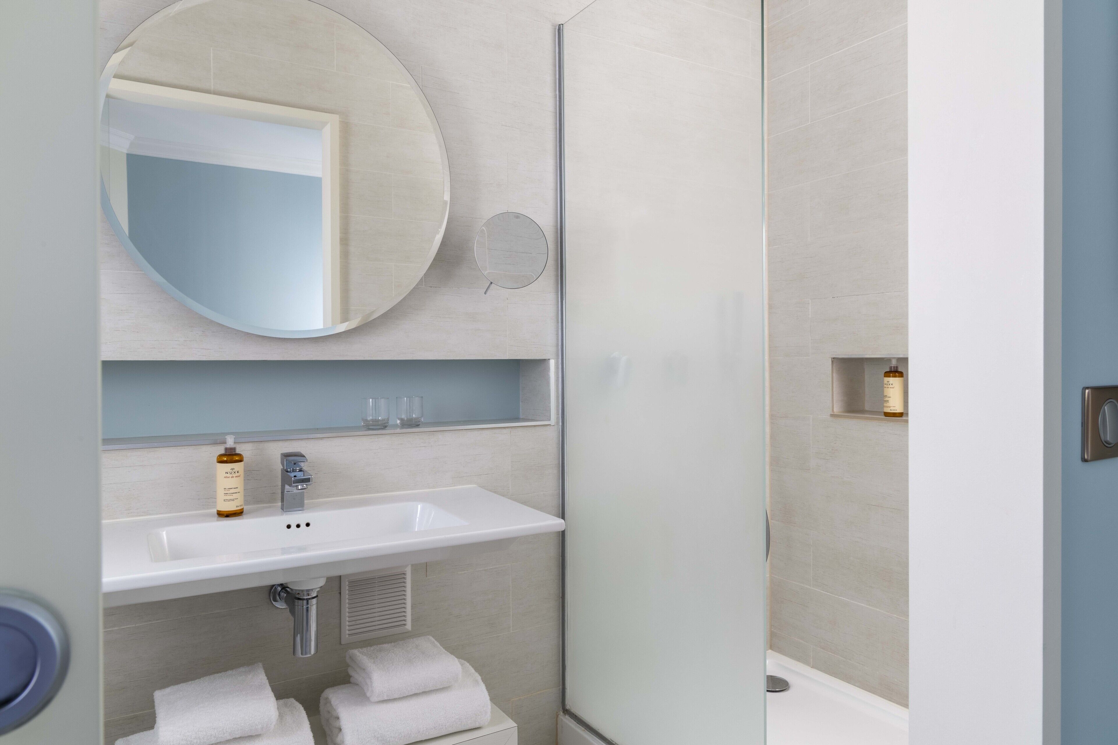A modern bathroom with a round mirror, a white sink, and a shower area.