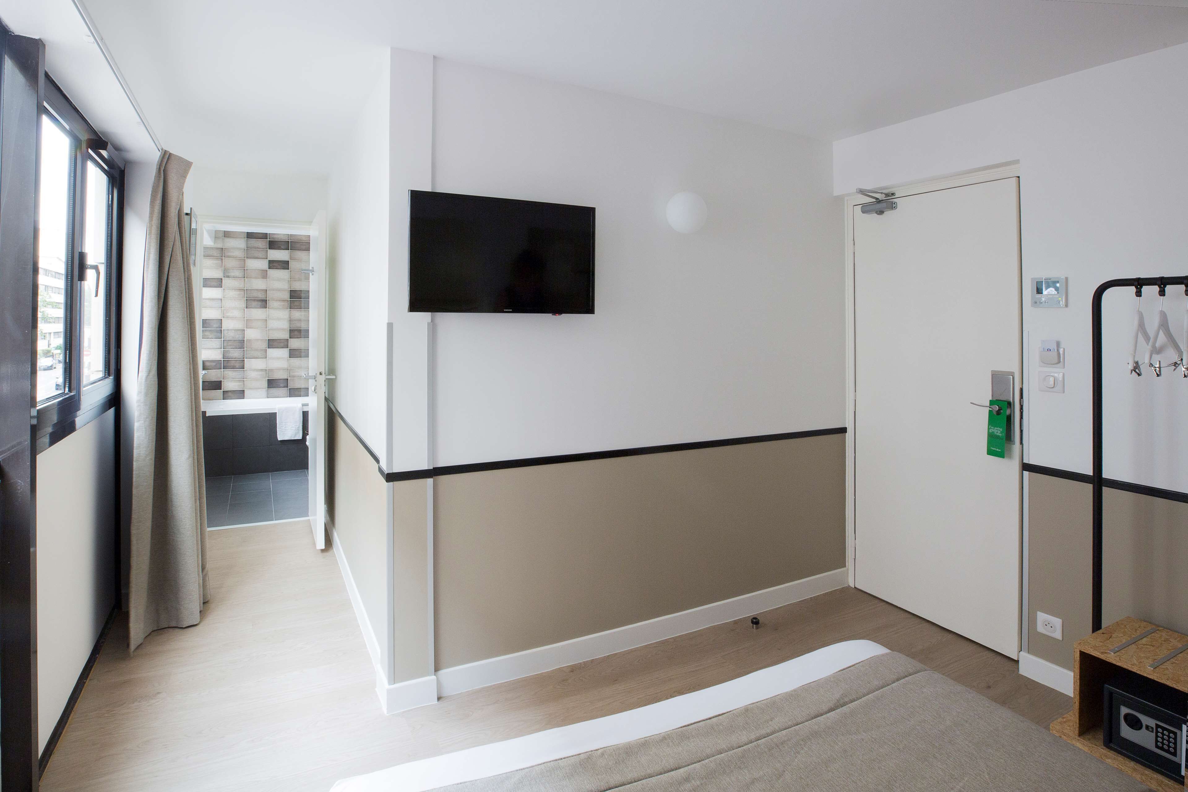 Une chambre d’hôtel dotée d’un téléviseur à écran plat fixé au mur, d’une porte équipée d’une serrure de sécurité et d’une petite table avec une radio.