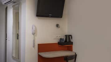 Una habitación pequeña con televisión montada en la pared, teléfono, cafetera y una silla.