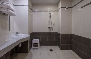 A modern bathroom with a sink, a shower, and a small stool.