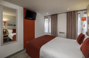 Camera d'albergo con un letto grande, una televisione a muro, uno specchio e una finestra con tende.