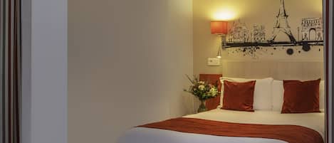 A hotel room with a bed, a nightstand, a lamp, a wall art of Paris landmarks, and a vase with flowers.