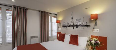 Una habitación de hotel con una cama grande, ropa de cama roja y blanca, un mural de París y una pequeña mesa con un jarrón de flores.