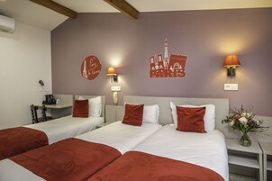 A hotel room with two beds, a desk, a telephone, and wall art depicting Paris landmarks.
