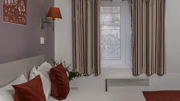 Une chambre d’hôtel avec un lit, des oreillers, une lampe, des rideaux et un radiateur.