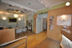 A reception area with a wooden reception desk, a seating area with chairs, a wall-mounted TV, and a decorative ceiling design.