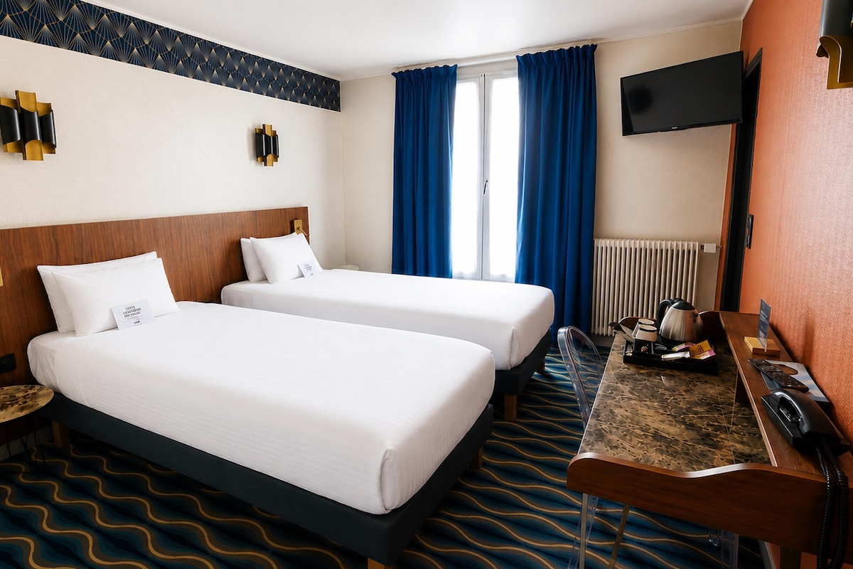 Une chambre d’hôtel avec deux lits, un bureau avec un téléphone et un téléviseur fixé au mur.