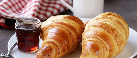 Two croissants on a plate with a cup of coffee and a jar of jam.