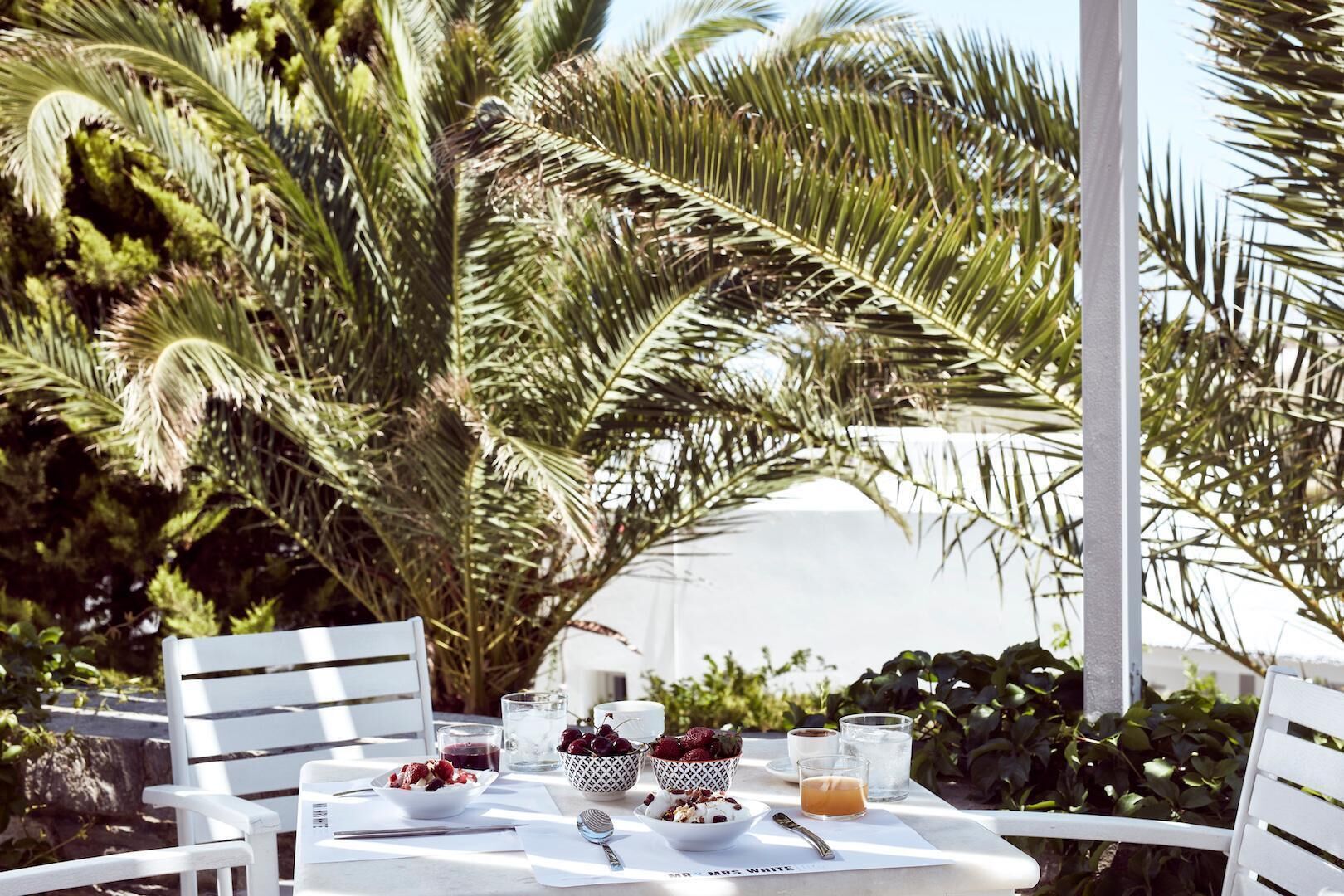Une table dressée à l’extérieur, avec vue sur des palmiers et un bâtiment en arrière-plan.