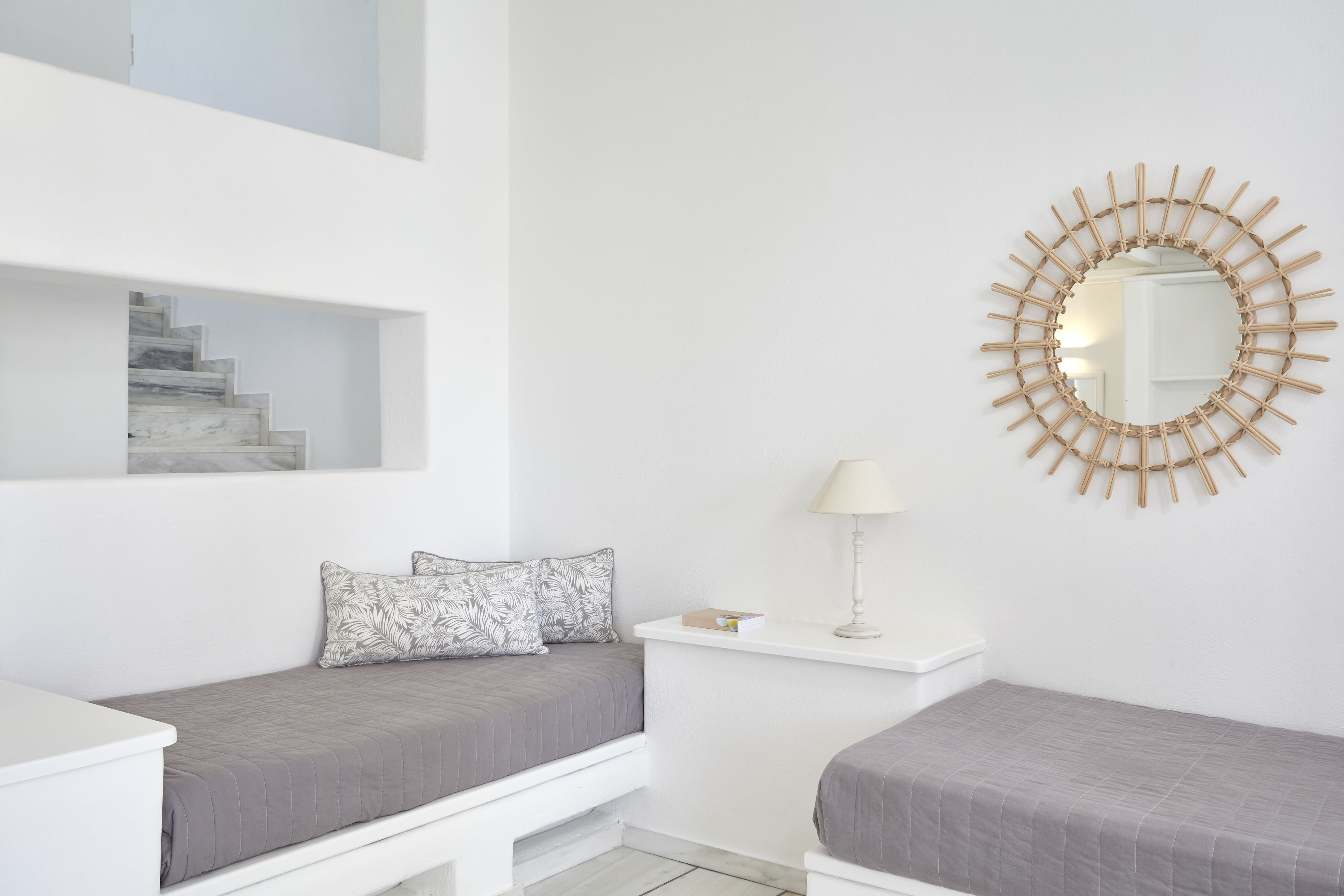 A bedroom with a bed, a nightstand, a lamp, a mirror, and a staircase.