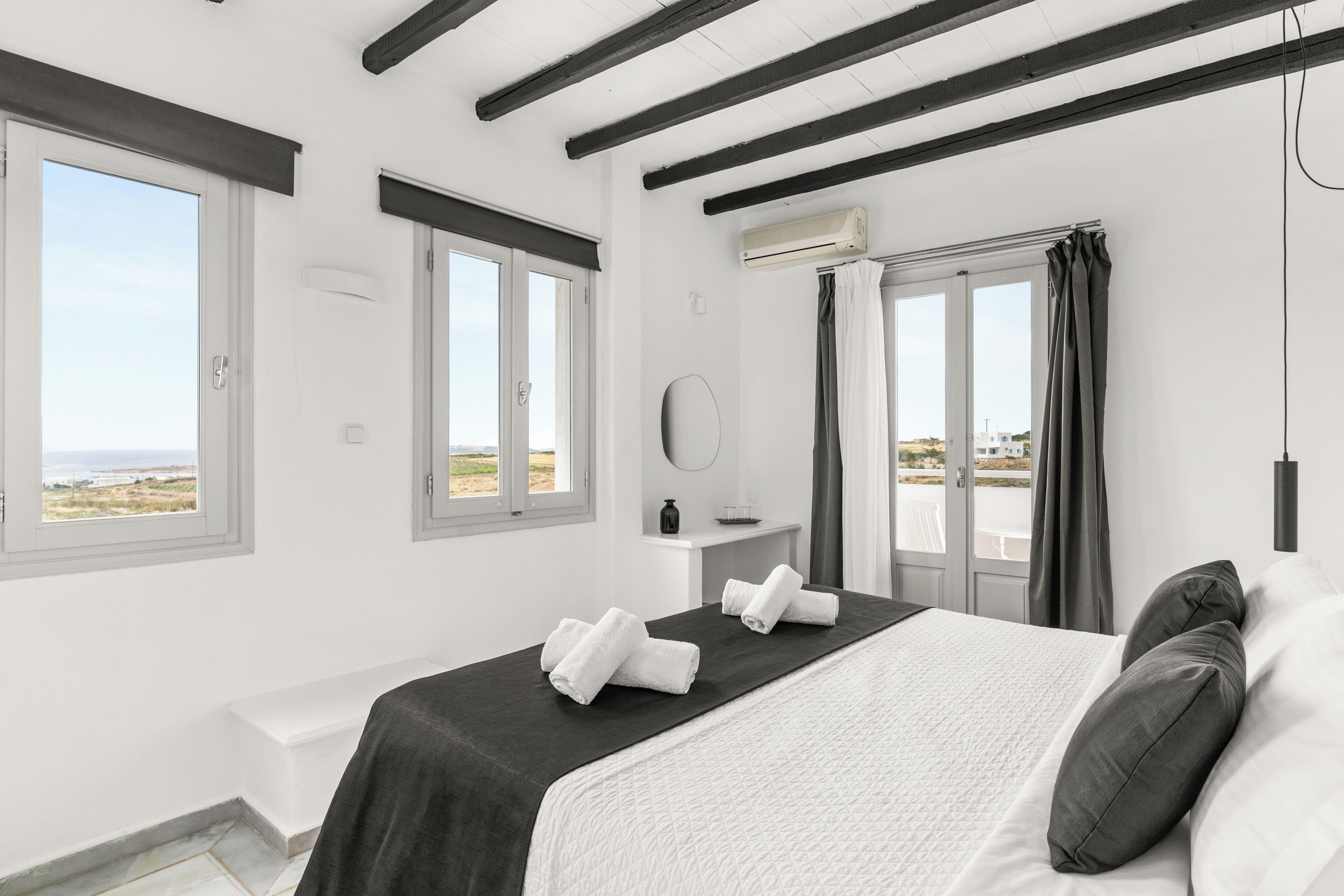 A bedroom with a bed, two windows, a door, and a view of the beach.