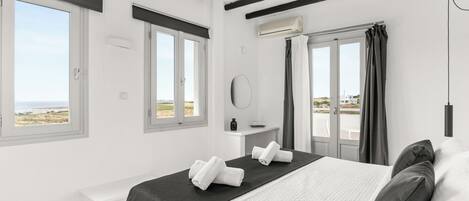 A bedroom with a bed, two windows, a door, and a view of the beach.