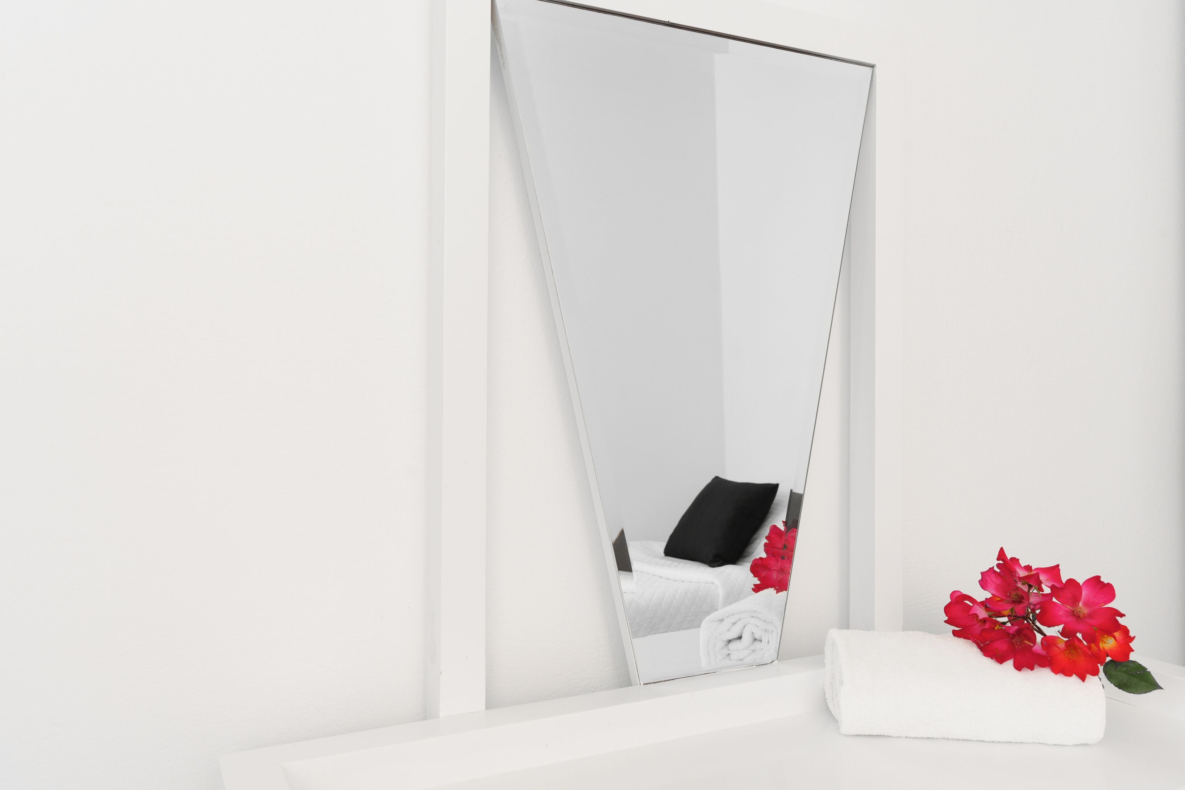 Un baño blanco con espejo, una toalla y flores rojas.