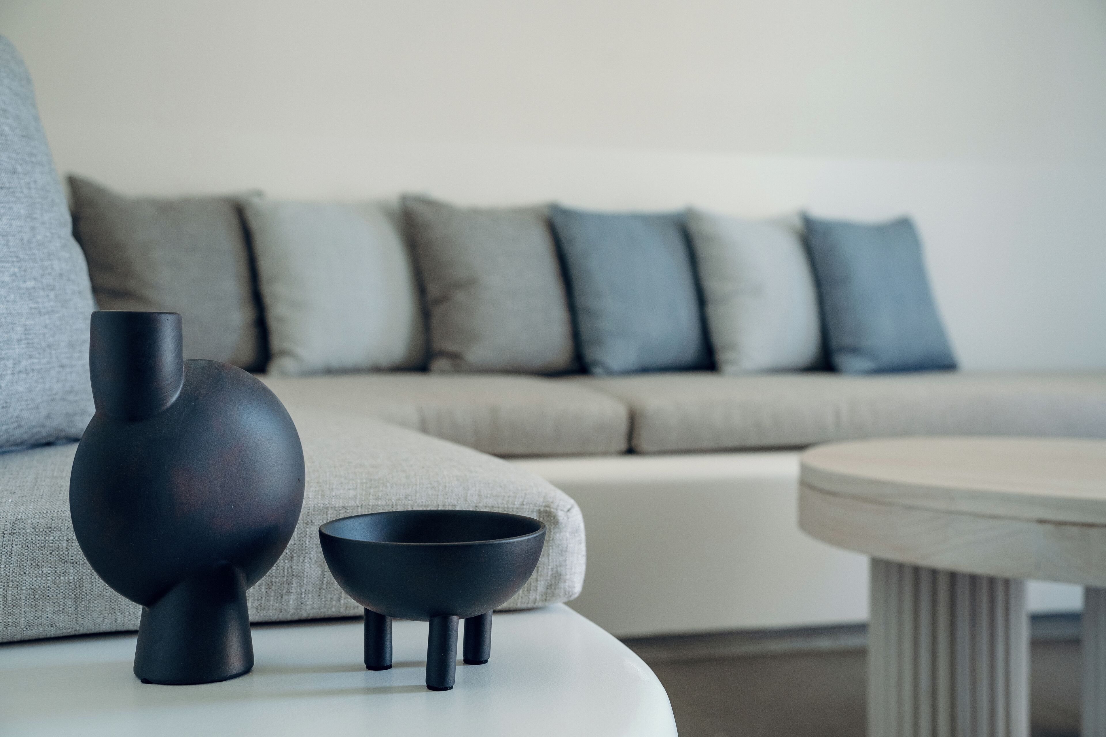 A modern living room with a grey sofa, a white coffee table, and two black decorative items.
