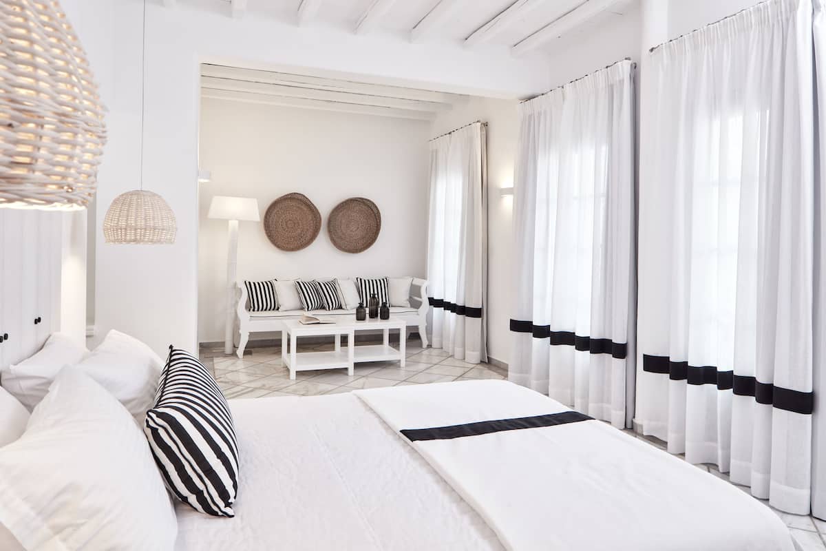 Un dormitorio moderno con una cama grande, un sofá y una mesita de centro. Hay cortinas en las ventanas y una lámpara colgante.