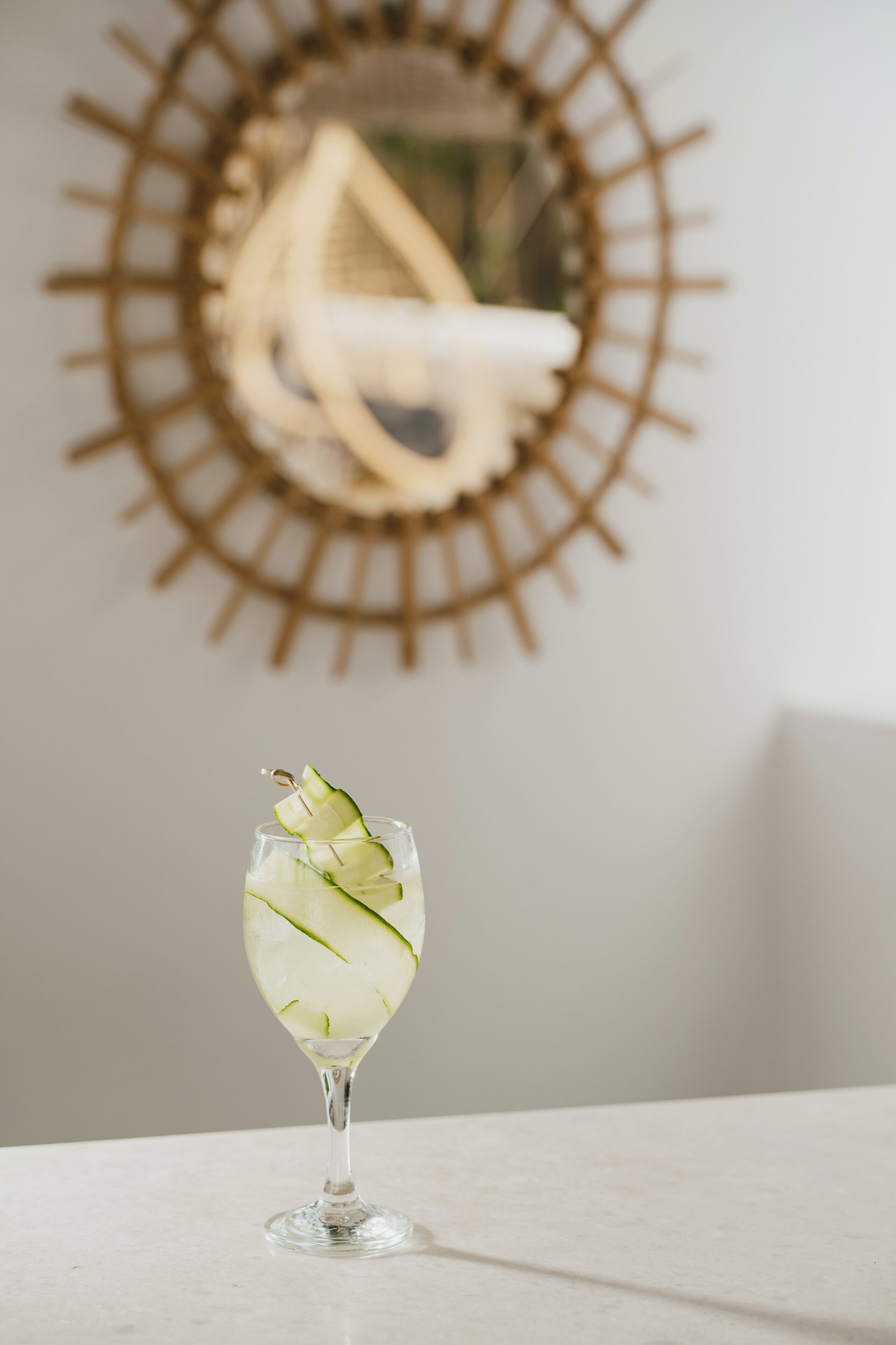 A clear glass with a drink garnished with cucumber slices on a marble surface.