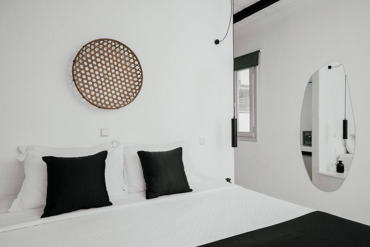 Una habitación de hotel moderna con una cama grande, dos almohadas negras, un adorno redondo en la pared, un espejo y una ventana.