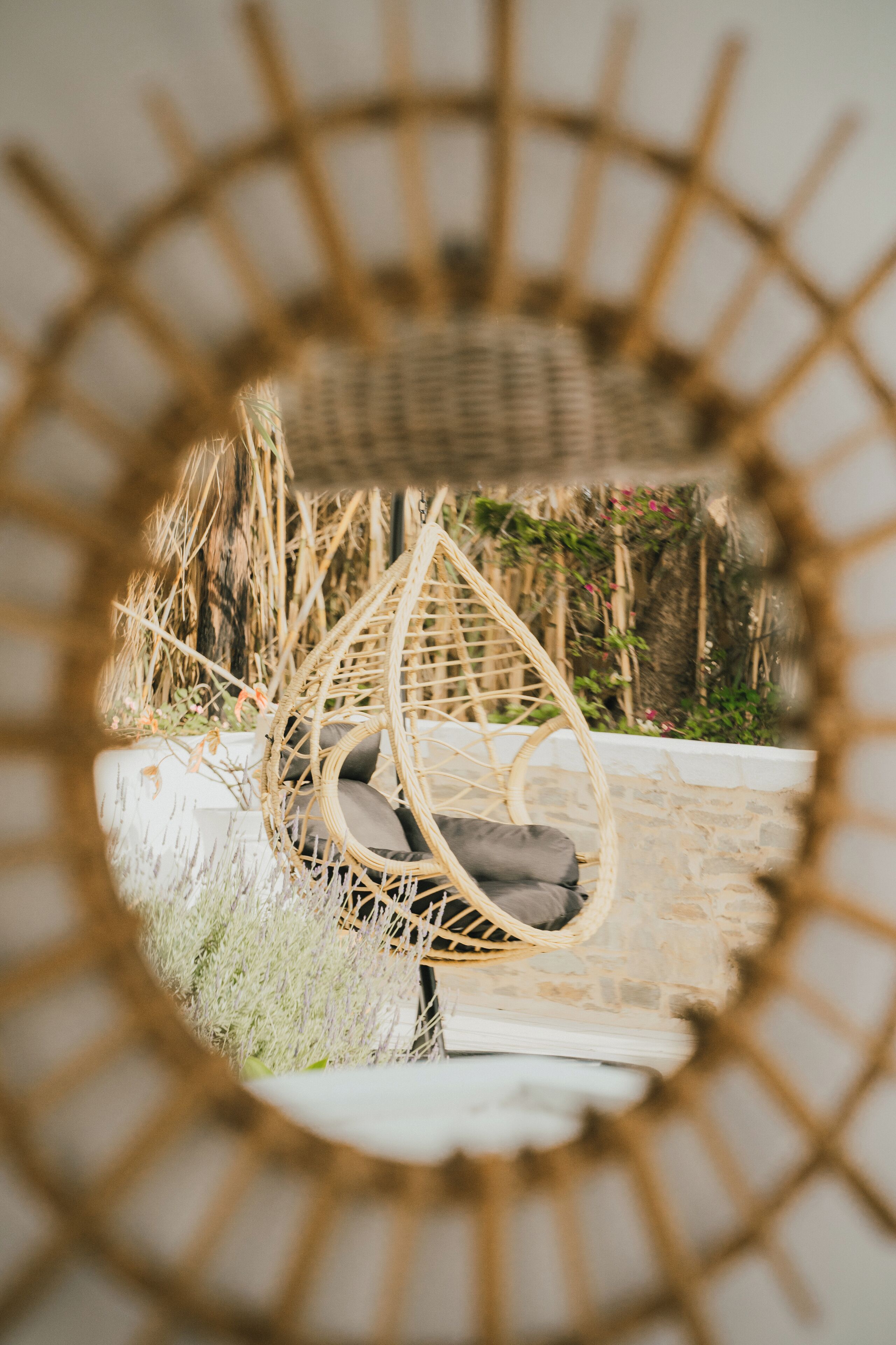 A wicker chair with a cushion, set against a stone wall and surrounded by plants.