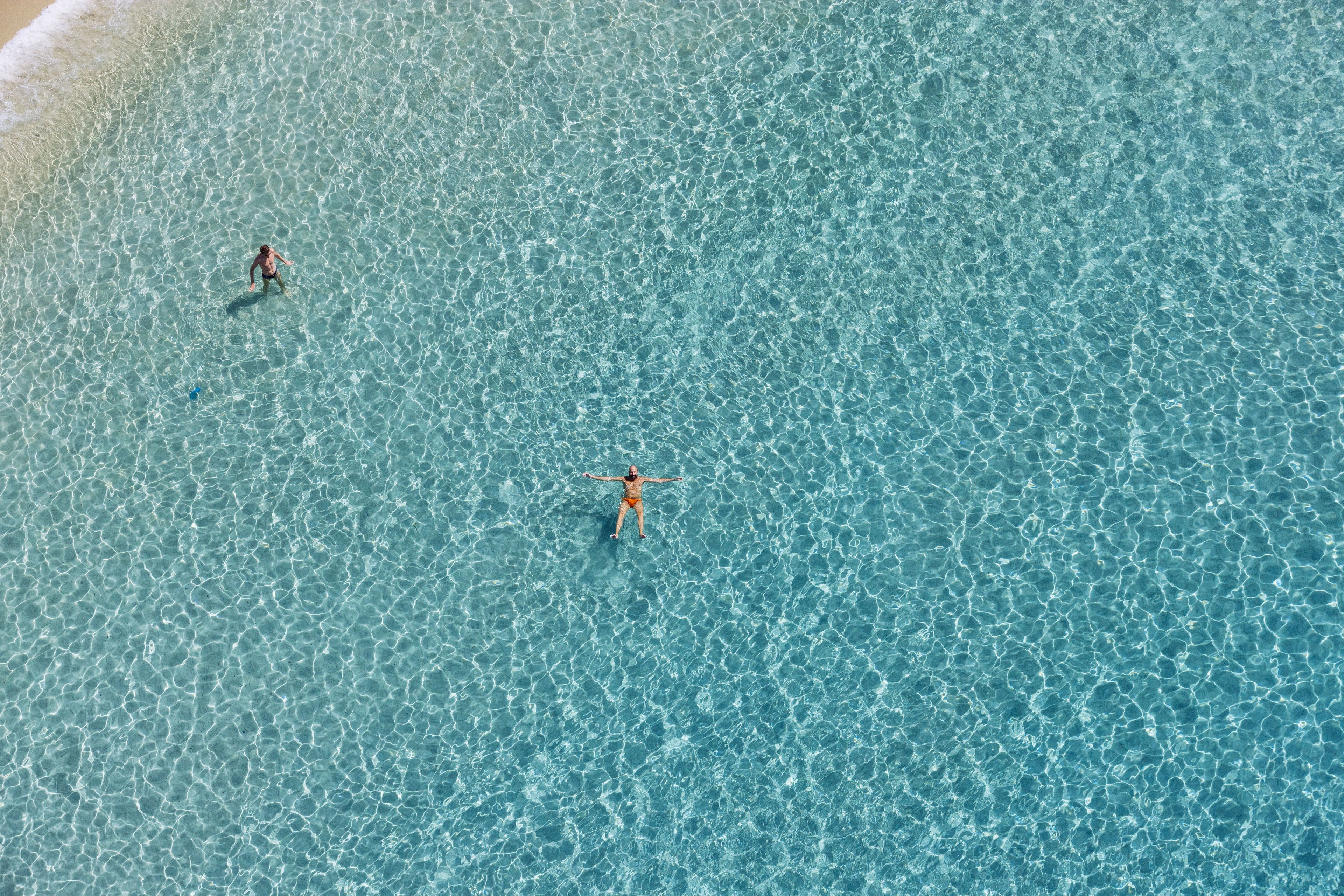 An aerial view of a beach with clear turquoise water and two people swimming.