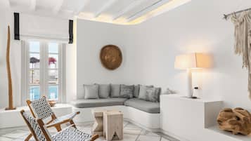Uma sala de estar moderna com um sofá seccional, uma poltrona estampada, uma mesa lateral de madeira e uma luminária fixa na parede.