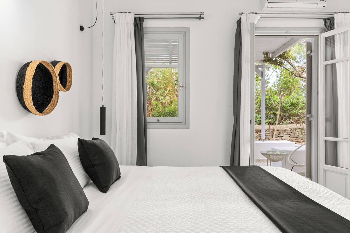 Un dormitorio con cama, dos almohadas, una mesita de noche y una ventana con cortinas.