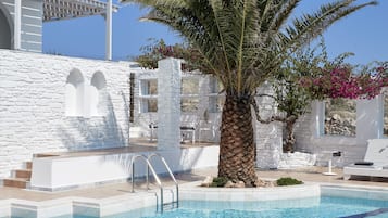 Una piscina con agua azul cristalina, rodeada de muros de piedra blanca y una palmera.