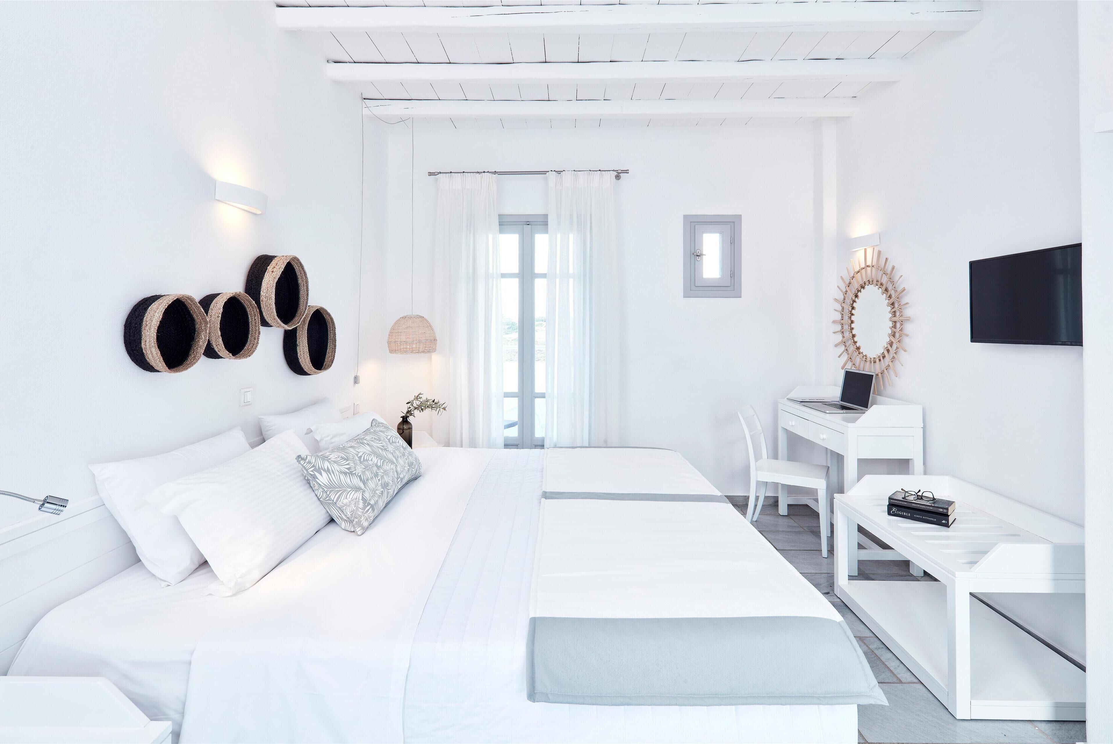 A modern, minimalist bedroom with a large bed, a desk, and a TV.