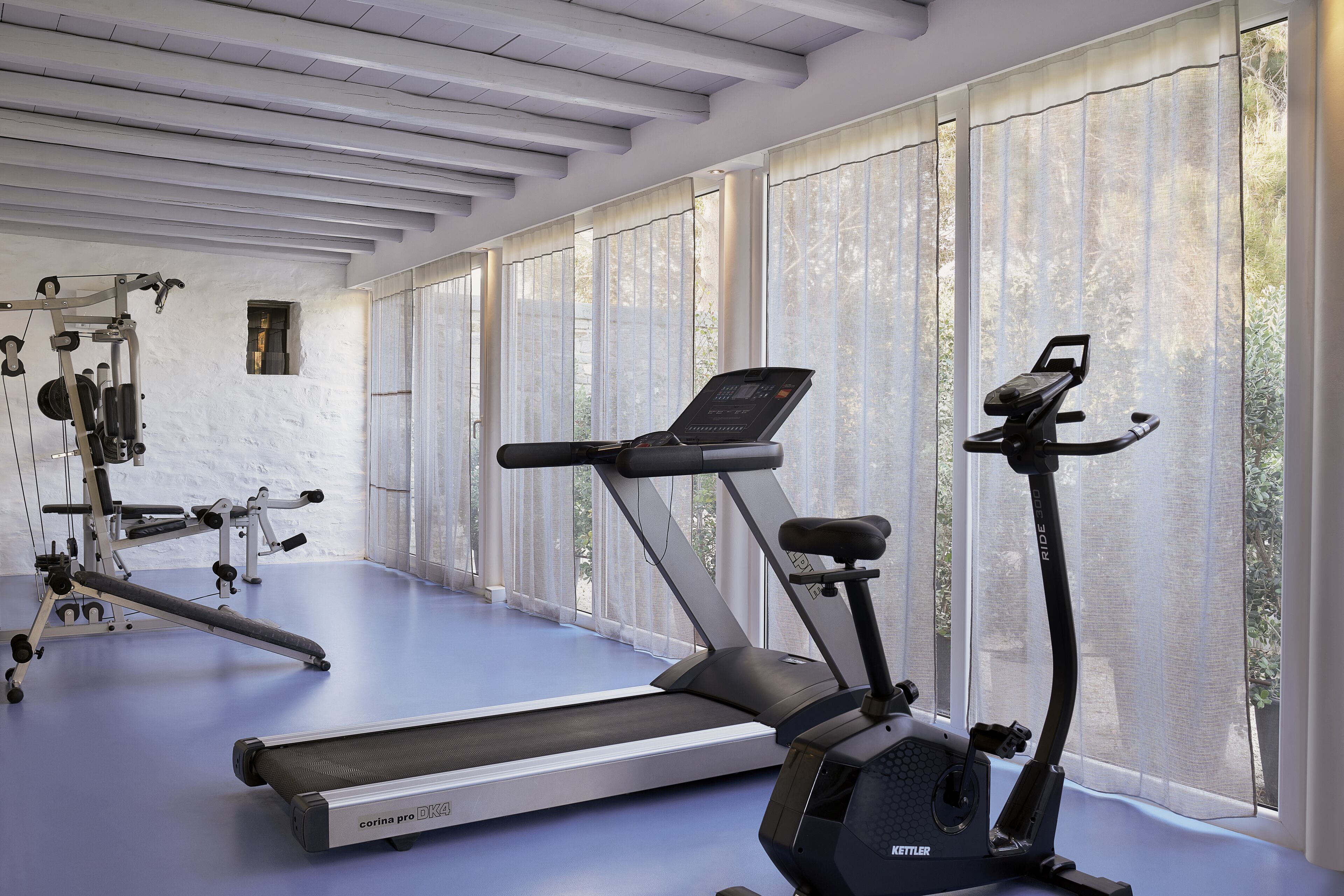 Une salle de sport équipée de machines de cardio, d’un rameur et d’une petite fenêtre.