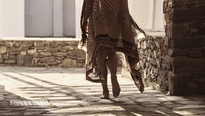 Une femme traverse un passage en arc, vêtue d’une robe à motifs et portant un chapeau.