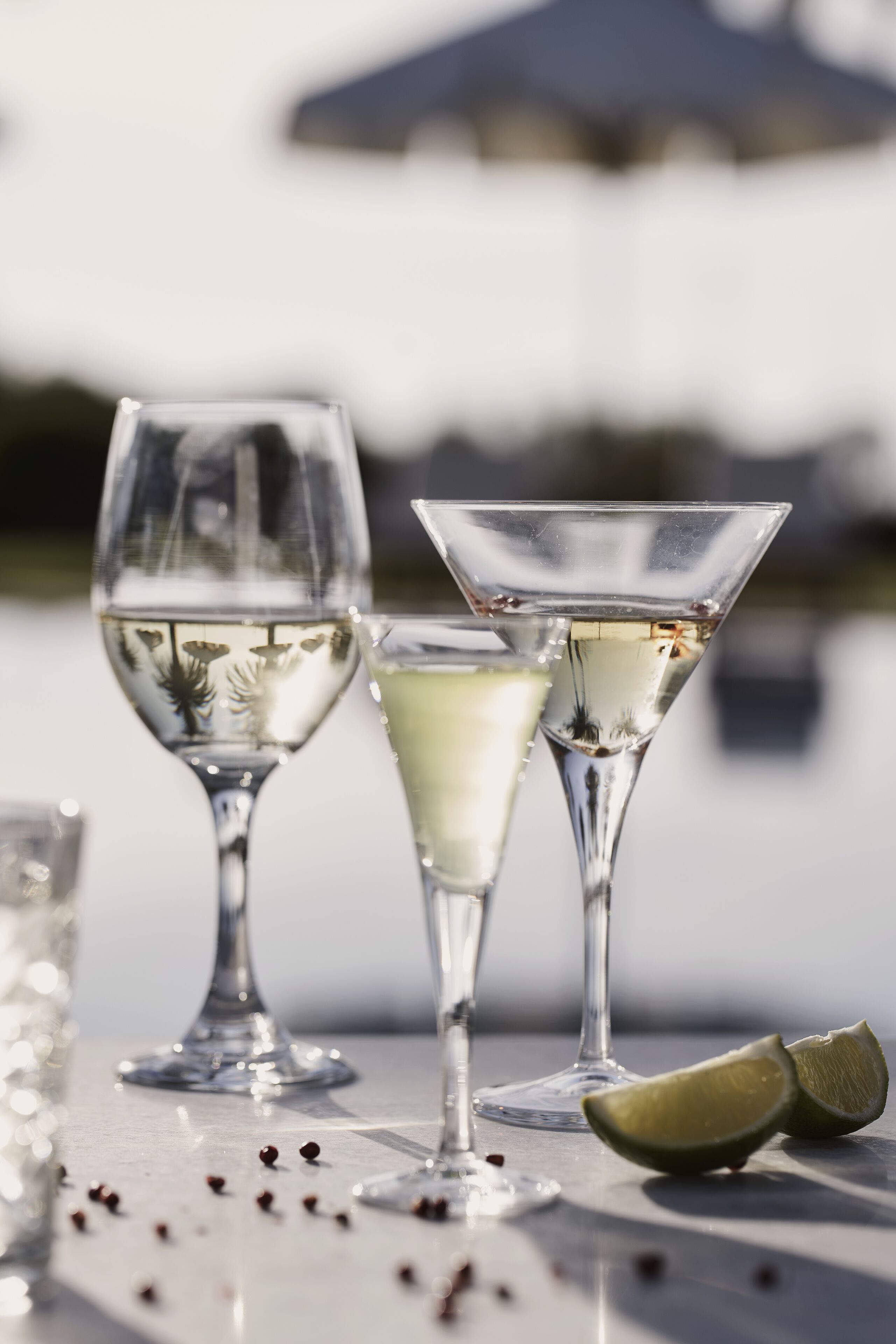 Three glasses of white wine on a table with a lime half, near a body of water.