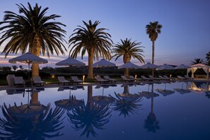 A poolside area with lounge chairs and umbrellas, palm trees, and a clear sky. - Yria Boutique Hotel & Spa (Paros)