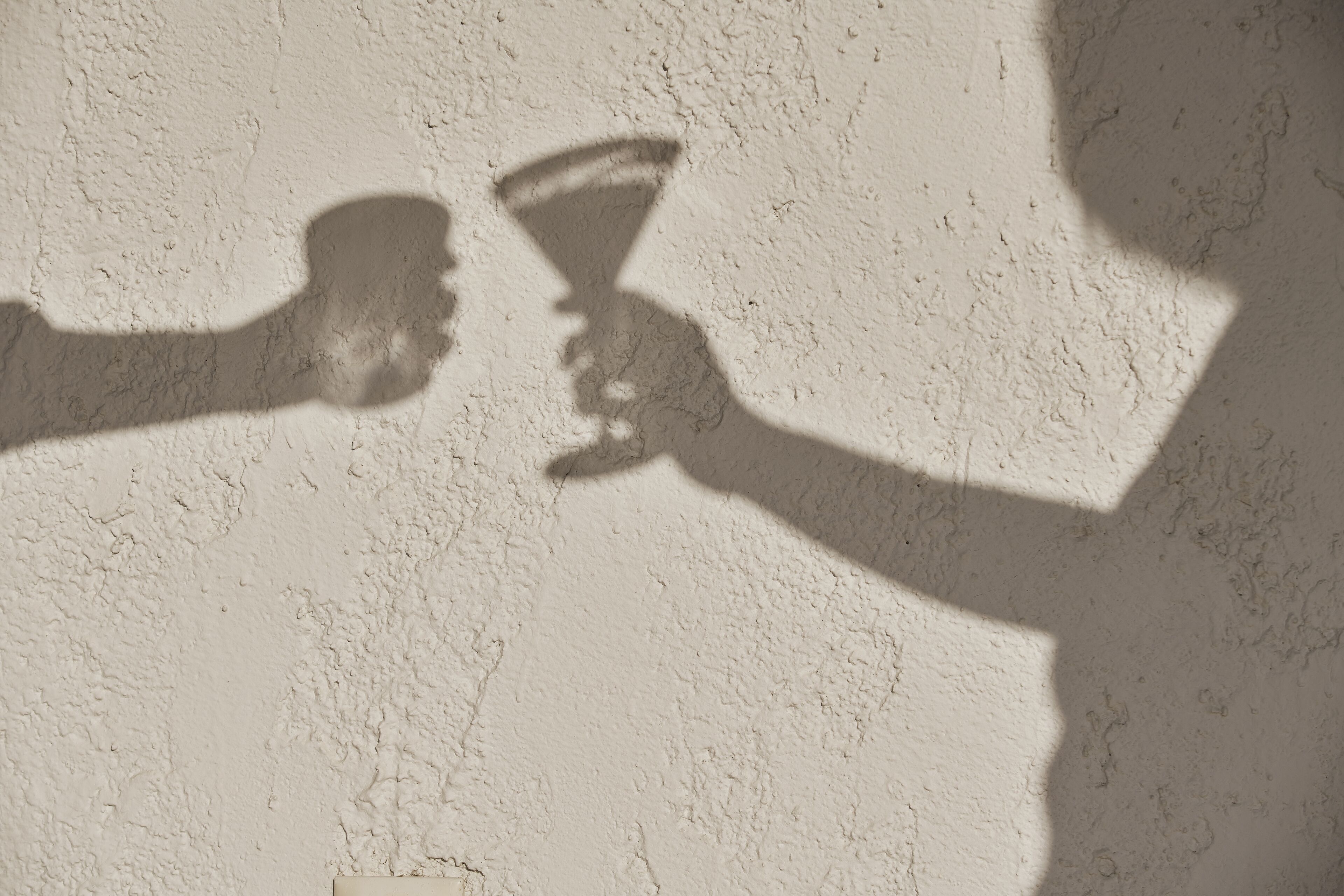 A textured wall with shadows of two people holding a glass.
