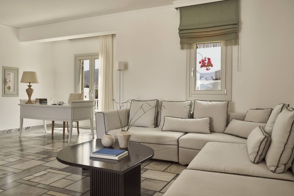 Un salon moderne avec un canapé beige, une table basse, un bureau et une fenêtre donnant sur un beau paysage.