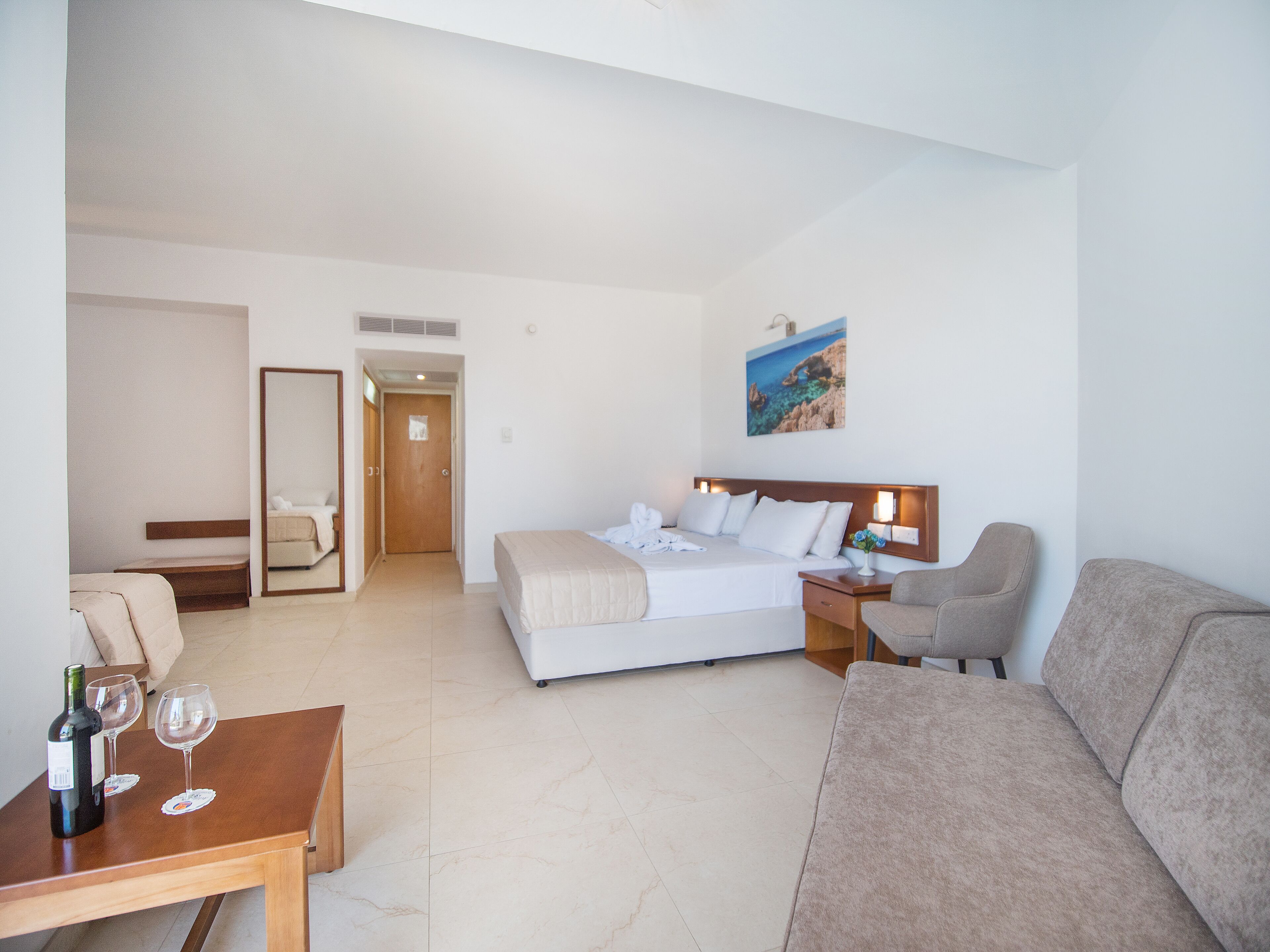 A hotel room with a bed, a sofa, a table with wine glasses, and a painting on the wall.
